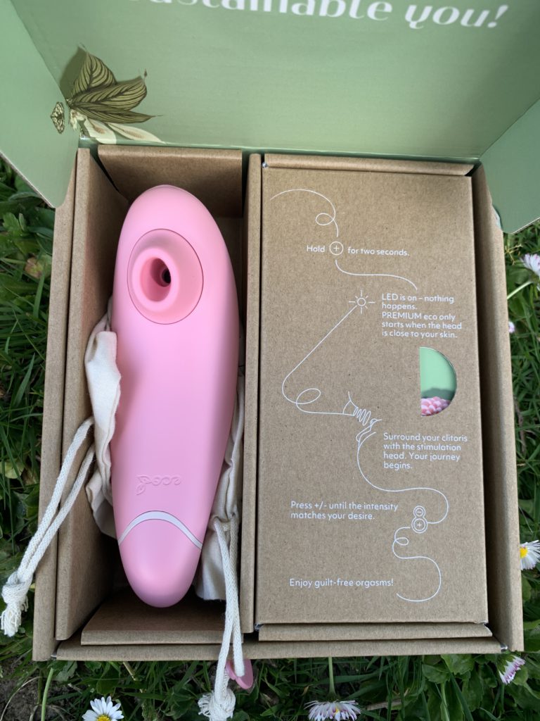 The Womanizer Premium Eco is pictured in its recycled box. It's a light pink color and comes with a charger, storage bag, and an additional head.