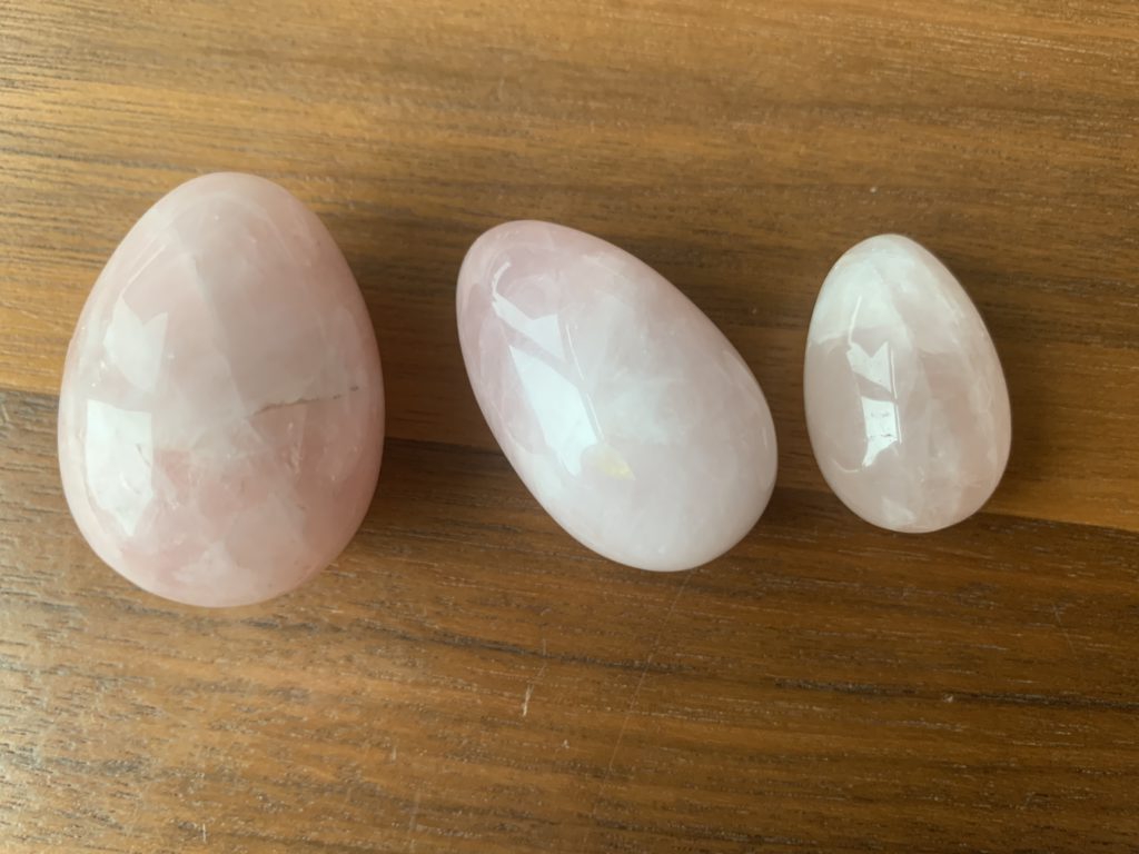 Rose quartz crystal yoni egg are pictured in three different sizes. Cracks are visible in one
