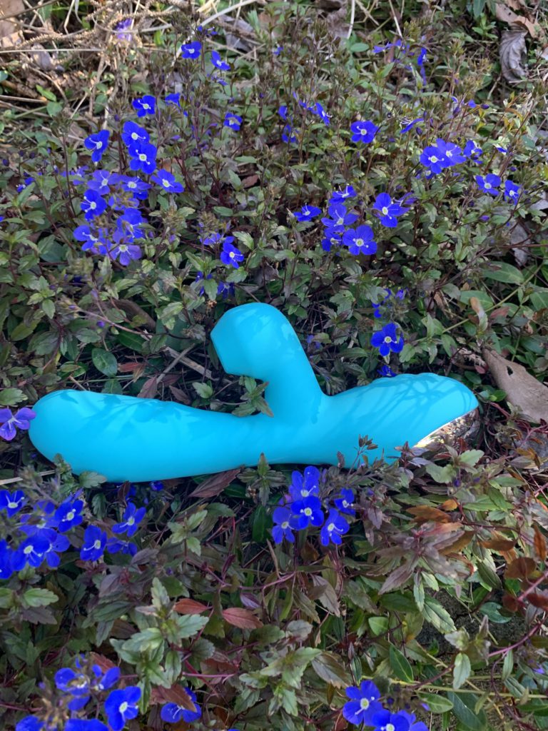 Caribbean Shine G-Spot Vibrator rests on a bush with lavender-colored flowers.