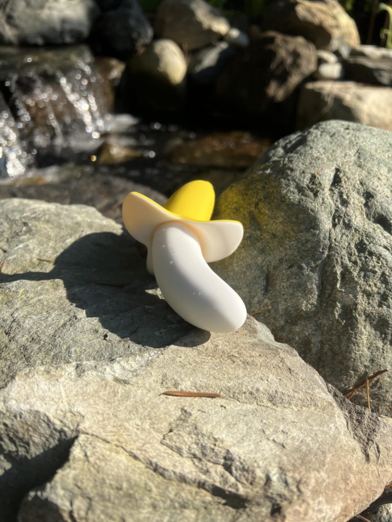 Half-Peeled Banana G-Spot Vibrator rests on a rock with a waterfall in the background
